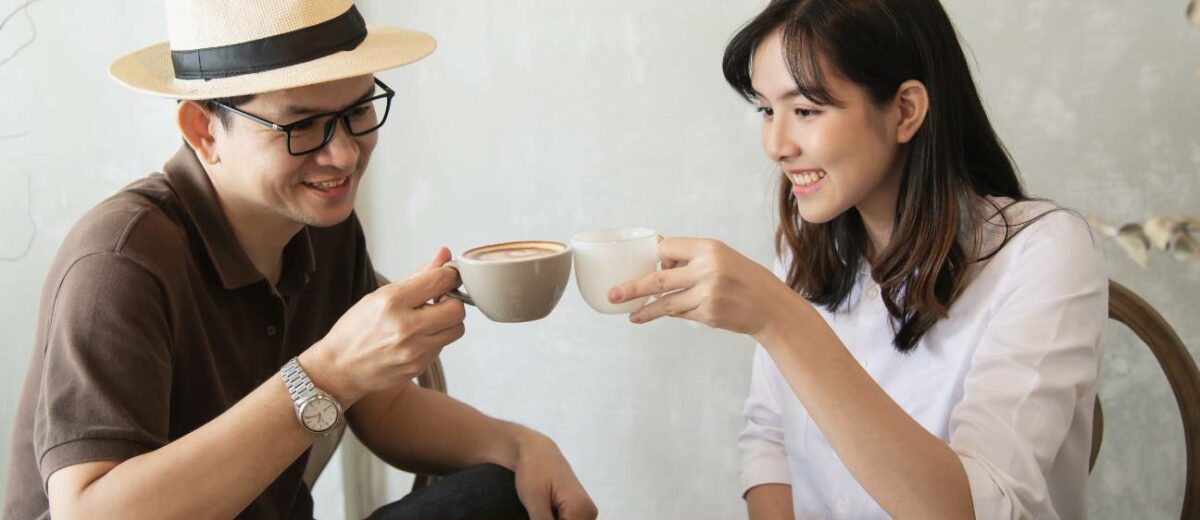 best coffee machine - Casual man in brown shirt and straw hat happily talking to woman in white blouse while drinking coffee at a table