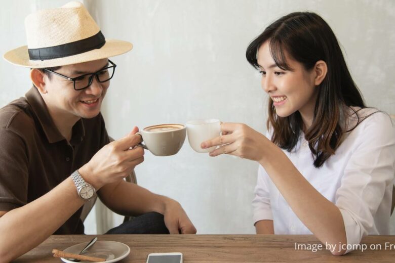 best coffee machine - Casual man in brown shirt and straw hat happily talking to woman in white blouse while drinking coffee at a table
