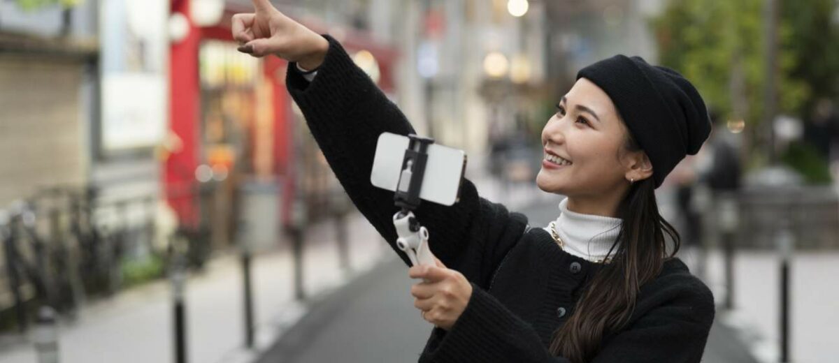 Young smiling female tourist vlogging with her smartphone on a gimbal stabilizer outdoors