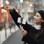 Young smiling female tourist vlogging with her smartphone on a gimbal stabilizer outdoors