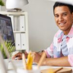 aesthetic work desk ideas - Smiling student in a pastel pink & blue checked shirt on a work desk