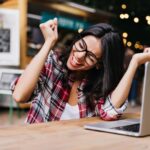 Wonderful female wearing glasses sitting in cafe with laptop, smiling and feeling happy