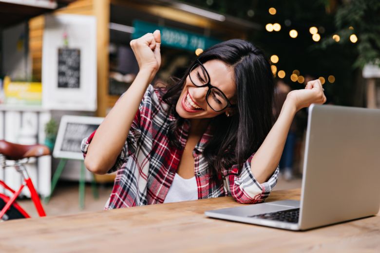 Wonderful female wearing glasses sitting in cafe with laptop, smiling and feeling happy