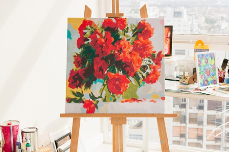 easel stand with a canvas paiting of red flowers in a vase